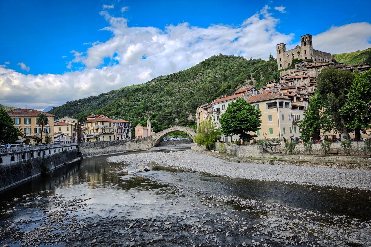 Dolceacqua, slikovita vasica v Liguriji, očara s svojo srednjeveško veduto, ki jo zaznamujeta stari kamniti most in mogočni grad Doria, ki se dviga nad ozkimi ulicami.